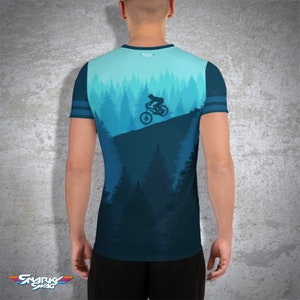 May include: A blue athletic t-shirt featuring a mountain biking scene. The design shows a cyclist riding downhill through a forest of pine trees. The shirt has blue stripes on the sleeves and the text "Snarky Swag" at the bottom.