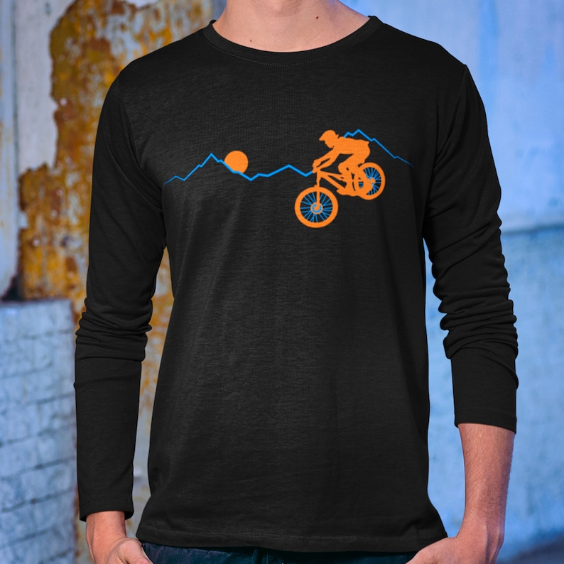 May include: Black long-sleeve t-shirt with an orange silhouette of a person riding a mountain bike over a blue mountain range with an orange sun in the background.