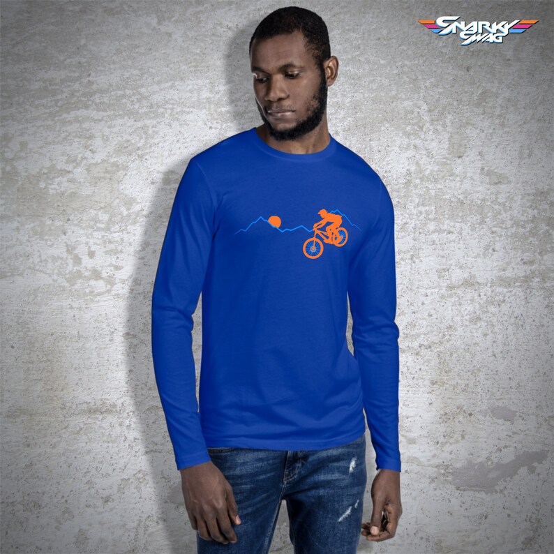 May include: A royal blue long-sleeve t-shirt with an orange silhouette of a person riding a mountain bike over a mountain range with a setting sun. The text "SNARKY SWAG" is in the upper right corner of the image.