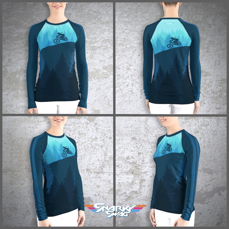 Peut inclure: Un t-shirt &agrave; manches longues avec un d&eacute;grad&eacute; de couleurs bleu et turquoise. Le t-shirt pr&eacute;sente une silhouette d'une personne faisant du v&eacute;lo de montagne dans une for&ecirc;t. Le t-shirt a une conception de manche raglan avec une bande bleu fonc&eacute; sur l'&eacute;paule.