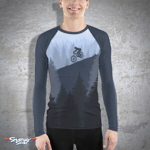 May include: A long-sleeved shirt with a dark blue base color and a light blue raglan sleeve design. The shirt features a graphic of a mountain biker riding through a forest.