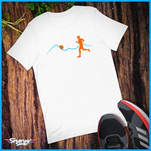 May include: White t-shirt featuring an orange silhouette of a person running on a blue mountain range with an orange sun in the background.