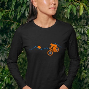May include: Black long-sleeve shirt with a graphic of a person riding a mountain bike in front of a sunset and mountains. The graphic is in orange and blue.
