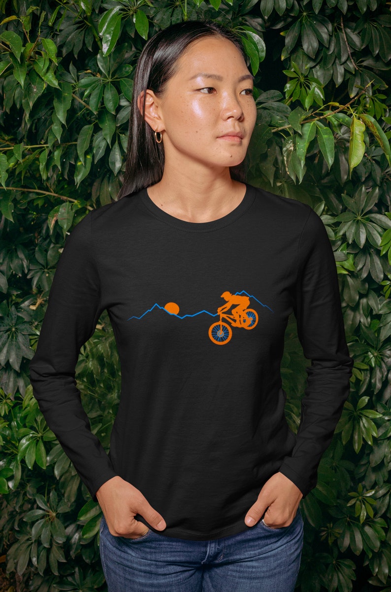 May include: Black long-sleeve shirt with a graphic of a person riding a mountain bike in front of a sunset and mountains. The graphic is in orange and blue.