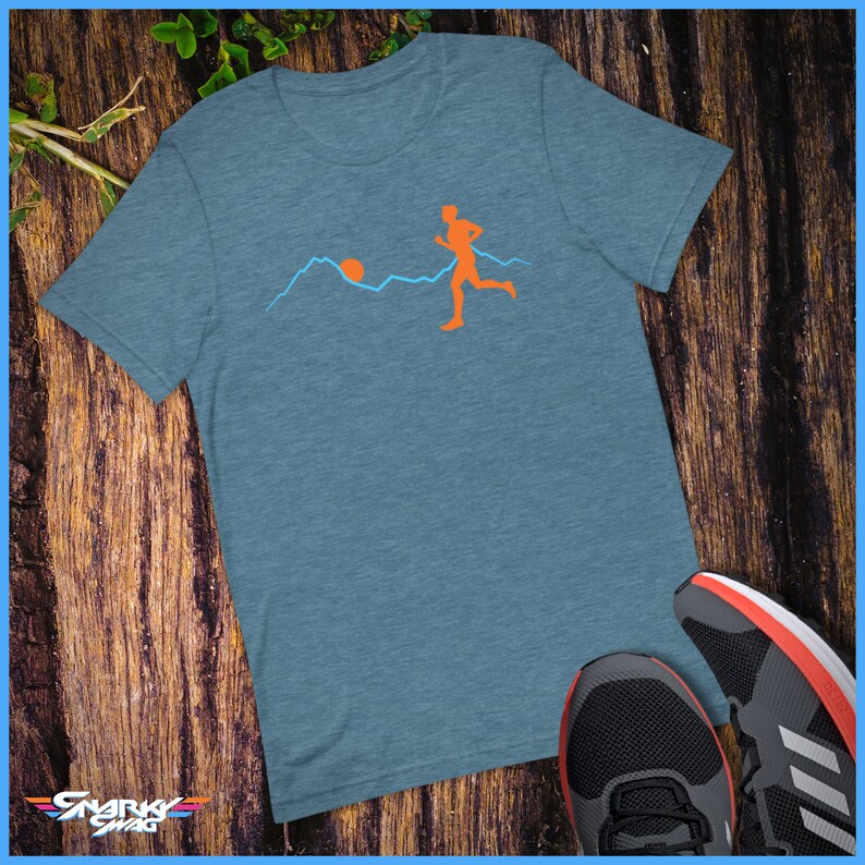 May include: A blue heather t-shirt featuring a graphic of a person running in front of a mountain range with a sun setting behind them.