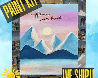May include: A paint kit featuring a landscape painting with mountains, a sun, and the text "free indeed." The mountains are blue and white, set against a pink and purple sky. The words "PAINT KIT" are in a yellow banner.