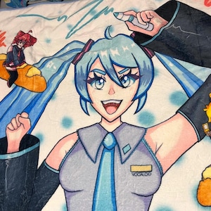 May include: A plush blanket featuring a vibrant anime-style illustration of a character with blue hair, a gray uniform, and a blue tie. The blanket includes additional cartoon figures and the word "VOCALOID".