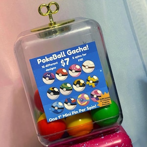 May include: A clear plastic gumball machine filled with colorful mini pin gacha balls. A blue sign reads "PokeBall Gacha!" with 12 different designs. The machine has a gold-colored key on top and contains 1-inch mini pins.