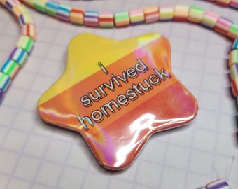 May include: A star-shaped badge with the text "I survived homestuck" in white lettering. The badge has a gradient of yellow to orange and a holographic sheen. Colorful beaded necklaces are in the background.