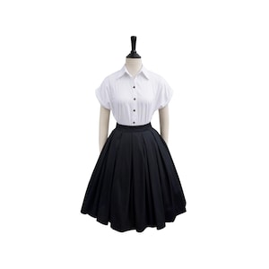 May include: A black skirt with a high waist and pleats. The skirt is on a mannequin wearing a white button-down shirt.