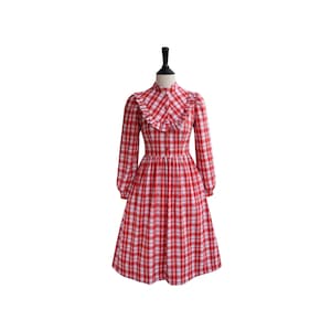 May include: A red and white plaid dress with a ruffled collar and long sleeves. The dress has a fitted bodice and a full skirt.