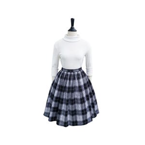 May include: A black and white plaid skirt with a high waist and a full, gathered skirt. The skirt is on a mannequin wearing a white turtleneck sweater.