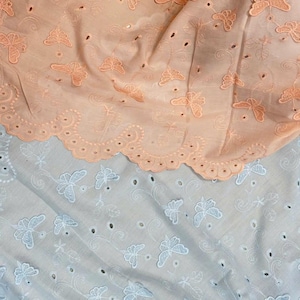 Puede incluir: Dos piezas de tela con un patrón de mariposa. La pieza superior es de color melocotón y la pieza inferior es blanca.