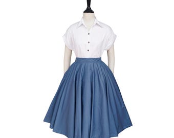 May include: A white short-sleeved button-down shirt paired with a denim blue, full, knee-length skirt. The skirt has a wide waistband and a flared silhouette. The outfit is displayed on a mannequin against a white background.