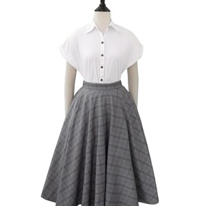 May include: A gray and white plaid skirt with a full circle shape. The skirt is on a mannequin wearing a white button-down shirt.