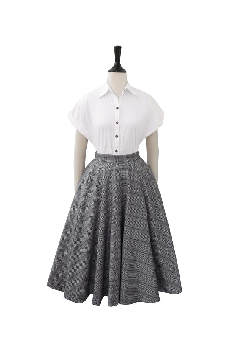 May include: A gray and white plaid skirt with a full circle shape. The skirt is on a mannequin wearing a white button-down shirt.