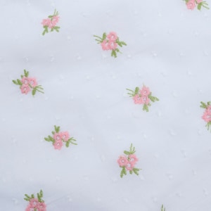 May include: White fabric with a delicate pattern of pink embroidered flowers. The fabric has a subtle texture.