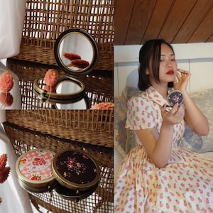 May include: Two vintage compact mirrors with floral and checkered designs. The mirrors are open and reflecting a wicker basket and a woman applying makeup.