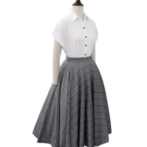 May include: A white button-down shirt with short sleeves and a gray and black plaid skirt. The skirt is full and has a high waist.