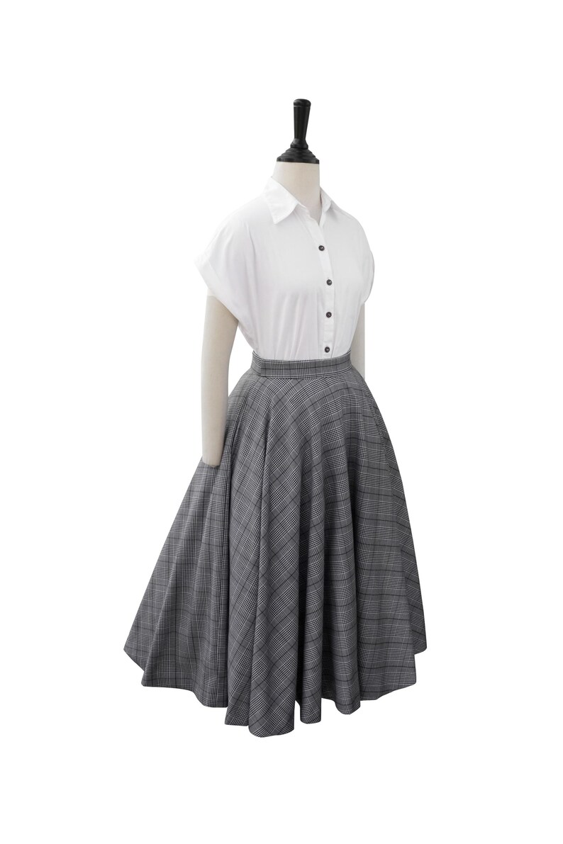 May include: A white button-down shirt with short sleeves and a gray and black plaid skirt. The skirt is full and has a high waist.