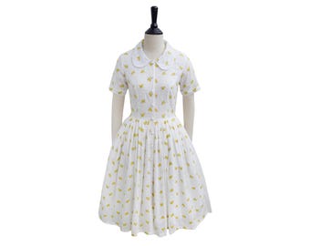 May include: A white dress with a yellow floral print and a Peter Pan collar. The dress has short sleeves and a full skirt.