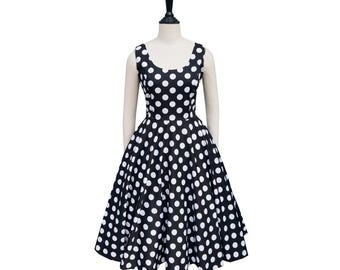 May include: A black and white polka dot dress displayed on a mannequin. The sleeveless dress features a scoop neckline and a full skirt. The white polka dots are evenly spaced on the black fabric. The dress is a classic vintage style.