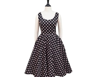 May include: A black sleeveless dress with a full skirt, adorned with pink polka dots. The dress is displayed on a mannequin, showcasing its classic, retro design. The dress has a scoop neckline and a fitted bodice.