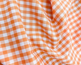 May include: Orange and white gingham fabric with a checkered pattern. The fabric is folded and has a soft, textured look.