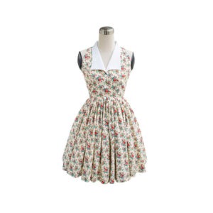 Op de afbeelding: Een mouwloze jurk met een witte kraag en een bloemenprint. De jurk heeft een getailleerd bovenstuk en een volle rok.