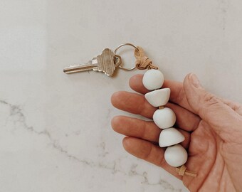 Chaveiro minimalista de porcelana com contas, estilo boho, perfeito para presentear em uma inauguração de casa ou como lembrancinha de fechamento de negócio imobiliário.