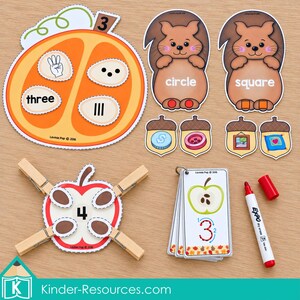 May include: Educational learning set featuring an orange pumpkin cutout with the number three, two squirrel cutouts labeled circle and square, four acorn cutouts, an apple cutout with four wooden clothespins, a set of flashcards, and a red dry erase marker.