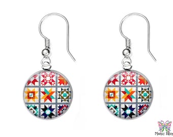 May include: A pair of silver earrings with a round, colorful, geometric pattern. The pattern is reminiscent of a quilt with various shapes and colors, including red, orange, yellow, green, blue, and black.
