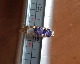 May include: A gold ring with two purple gemstones. The ring is being measured with a ruler, and the measurement is 18.