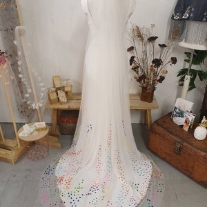 May include: A white tulle wedding veil with a rainbow of colorful dots on the bottom edge.