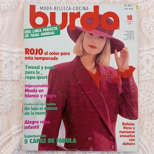 Può includere: Una copertina di rivista Burda vintage con una donna che indossa un blazer rosso e un cappello a tesa larga. Il titolo della rivista è "Burda" in grandi caratteri grassetto. Il testo della copertina include "ROJO el color para esta temporada" e "5 CAPAS DE FABULA".