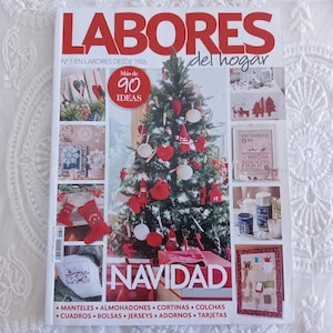May include: A magazine titled Labores del hogar featuring a Christmas theme on the cover. The cover displays a decorated Christmas tree with red ornaments, surrounded by smaller images of holiday crafts, including stockings and embroidered items.