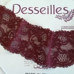 Peut inclure: Bordure en dentelle de couleur bordeaux avec un motif floral délicat. La bordure est présentée sur un fond blanc avec le texte "Desseilles" et "Composition" imprimé sur le fond.