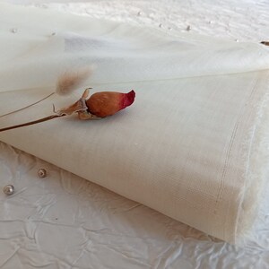 May include: A white sheer fabric with a slightly rough texture. The fabric is folded in half and has a raw edge. There are dried flowers and beads on the surface.