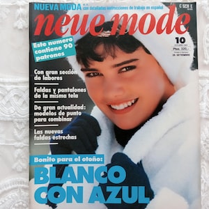 Może przedstawiać: Okładka magazynu w stylu vintage z czerwonym tytułem "neue mode". Na okładce uśmiechnięta osoba w białym płaszczu z kapturem i granatowych rękawicach. Widoczny jest tekst "BLANCO CON AZUL" oraz inne teksty w języku hiszpańskim.