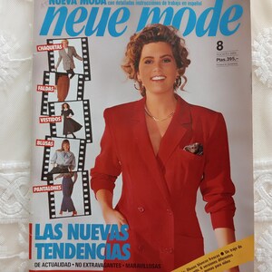 Puede incluir: Una portada de revista "neue mode" con el número 8. Presenta a una mujer con una blazer roja e imágenes de ropa. El texto incluye "LAS NUEVAS TENDENCIAS" y detalles sobre chaquetas, faldas, vestidos, blusas y pantalones.