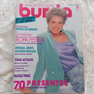 Puede incluir: Una portada de revista con una mujer que lleva una chaqueta de color turquesa y un top morado. La revista se titula "Burda" y presenta el texto "70 Presentes Preciosas labores".