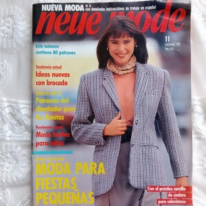 Può includere: Una copertina di rivista con il titolo "Nueva Moda" in rosso e la parola "neue mode" in rosso. La copertina presenta una donna con un blazer a quadri e una sciarpa. La rivista include testo in spagnolo, tra cui "Moda para fiestas pequeñas."