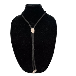 May include: A black bolo tie with a white seashell accent. The tie is on a black velvet mannequin bust.