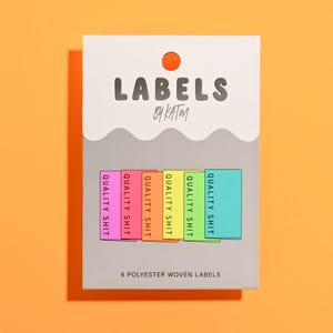 May include: A rectangular white and gray cardboard packaging containing six colorful polyester woven labels. The text LABELS BY KATM is printed at the top, and the labels are displayed in pink, orange, yellow, green, and teal with the text QUALITY SHIT.