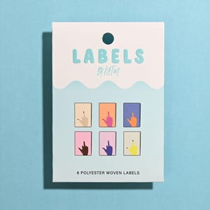 May include: A rectangular package of 6 polyester woven labels with the text LABELS BY KATM at the top. The packaging features a light blue and white design with six small rectangular illustrations of hands making a middle finger gesture.