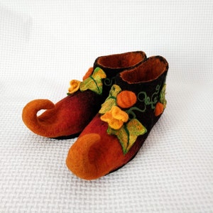 May include: A pair of orange and brown felt slippers with a pointed toe and a pumpkin design. The slippers have green leaves and orange pumpkins embroidered on them.