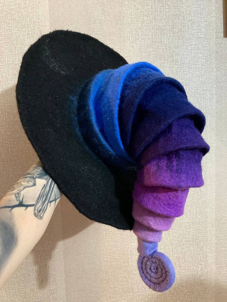 May include: A purple and blue gradient witch hat with a curled brim and a pointed top. The hat is made of felt and has a black base.