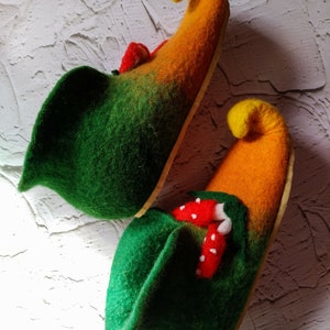 May include: A pair of green and orange felt slippers with pointed toes. The slippers have a whimsical design with red and white mushroom accents.