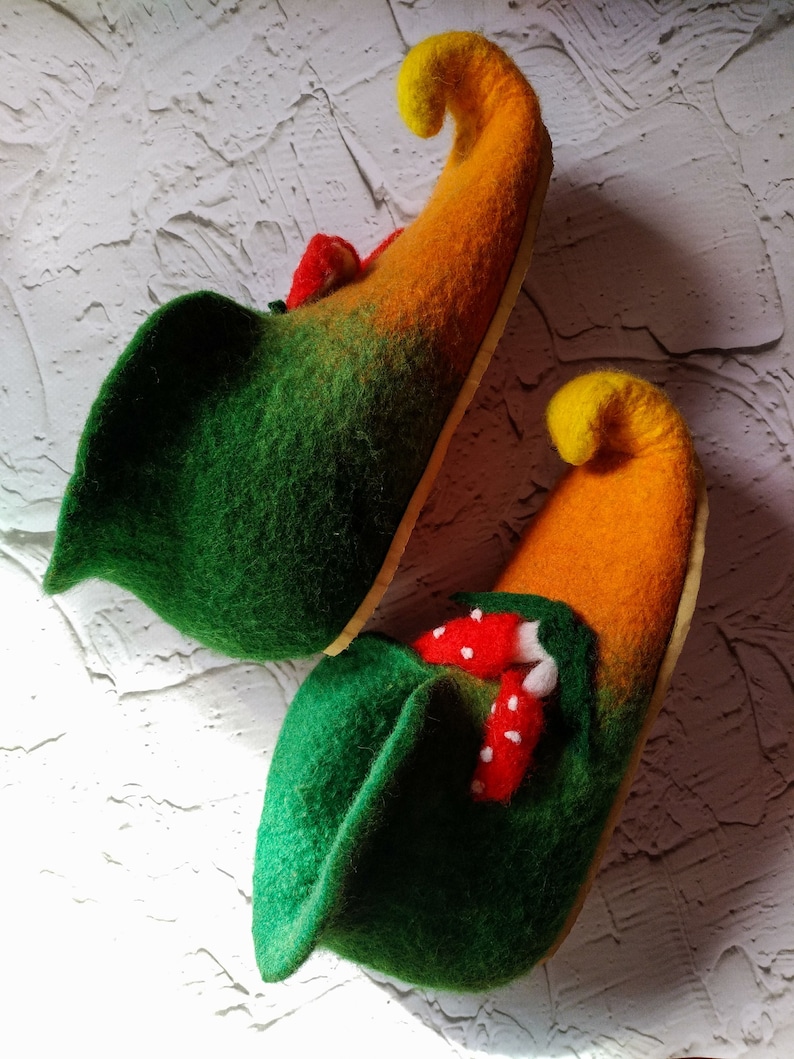 May include: A pair of green and orange felt slippers with pointed toes. The slippers have a whimsical design with red and white mushroom accents.