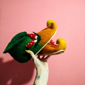 May include: A pair of green and orange felt slippers with pointed toes. The slippers are decorated with red and white felt mushrooms.